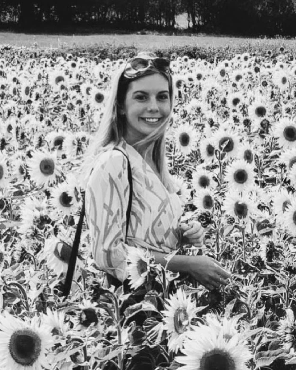Katie smiling, standing in a field of sunflowers.